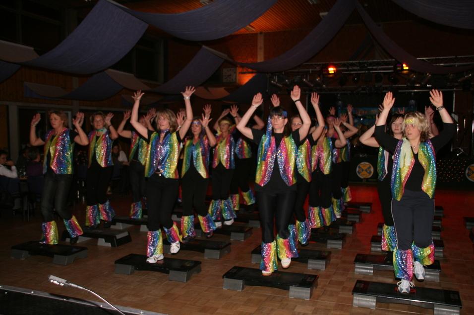 Gruppe von Tänzerinnen in bunten Kostümen, die auf Steppbrettern in einem festlich dekorierten Raum tanzen.